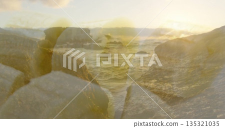 Bathing rocky outcrop and waves in golden light from sun near horizon at shoreline, with boulders 135321035