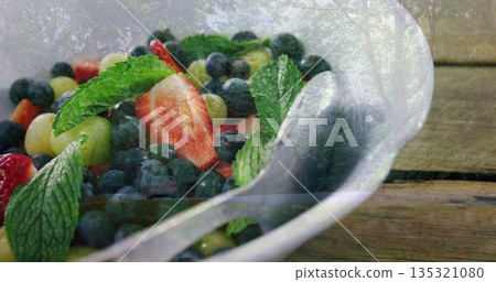 Displaying white bowl holding fresh berries, grapes and mint leaves on rustic tabletop with spoon 135321080