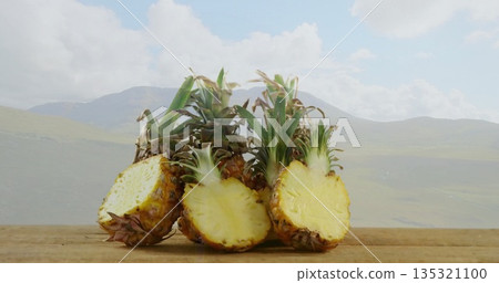 Displaying cluster of four pineapples arranged on wooden table outdoors, with mountain backdrop 135321100