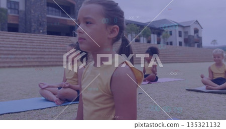 Sitting girls meditating in grassy courtyard, with yoga mats, yellow tops and black shorts 135321132