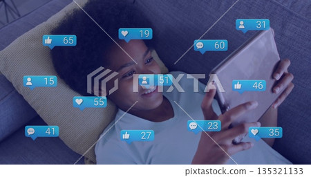 Browsing teenage girl holding tablet and checking floating like icons on gray sofa, tablet computer Browsing teenage girl holding tablet and checking floating like icons on gray sofa, tablet computer 135321133