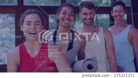 Smiling friends standing in fitness studio overlooking garden, holding rolled exercise mats 135321151