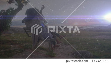 Cuddling couple watching sunset on park bench at coastal park with overhead branch and rocky shore 135321162