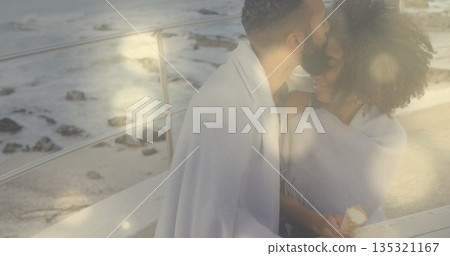 Kissing couple holding ice cream in blanket against metal railing on coastal walkway, copy space 135321167
