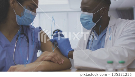 Injecting doctor administering vaccine into nurse in scrubs' arm at clinic, with syringe and vials 135321235