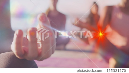 Holding woman's hand in meditation mudra on yoga mat at beach water's edge, with dawn glow 135321270