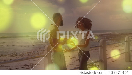 Standing couple holding hands on seaside promenade at sunset, with metal railing and ocean waves Standing couple holding hands on seaside promenade at sunset, with metal railing and ocean waves 135321405