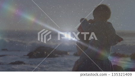 Standing mother holding toddler on rocky shoreline at sunset, wearing jackets, copy space Standing mother holding toddler on rocky shoreline at sunset, wearing jackets, copy space 135321409