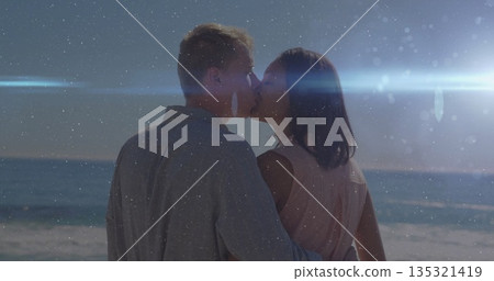 Kissing couple wearing dress and shirt on sandy shore during dusk, with pastel haze flare 135321419