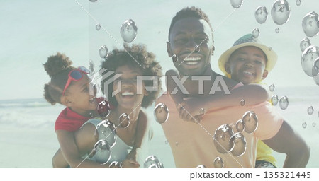 Smiling family carrying children on backs at sandy seashore, with straw sun hat and red sunglasses Smiling family carrying children on backs at sandy seashore, with straw sun hat and red sunglasses 135321445