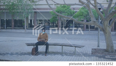 Man wearing medical mask sitting on wooden bench in courtyard, with tablet, leather bag 135321452