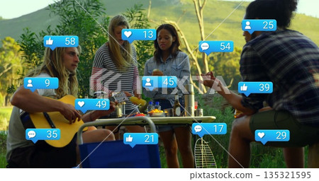 Group of friends playing guitar and sharing snacks in grassy meadow, with collapsible picnic table Group of friends playing guitar and sharing snacks in grassy meadow, with collapsible picnic table 135321595
