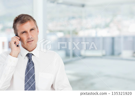 Mature man standing in striped tie holding smartphone by column near window in office, copy space Mature man standing in striped tie holding smartphone by column near window in office, copy space 135321920