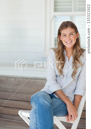 Adult woman sitting on porch chair smiling at camera with shuttered window behind Adult woman sitting on porch chair smiling at camera with shuttered window behind 135321922