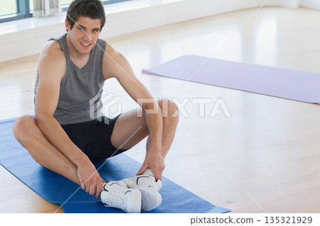 Man stretching on blue mat in fitness studio near purple mat and white sneakers, copy space 135321929