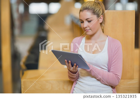 Woman sitting on wooden bench in lecture hall, holding tablet device and leaning back, copy space 135321935