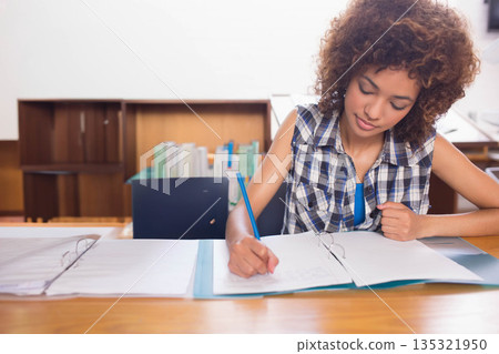 Female student writing notes in notebook with blue pencil amid open binders, laptop in study room Female student writing notes in notebook with blue pencil amid open binders, laptop in study room 135321950