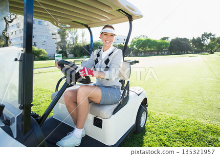 Senior woman sitting in golf cart on fairway gripping steering wheel wearing visor and golf glove Senior woman sitting in golf cart on fairway gripping steering wheel wearing visor and golf glove 135321957