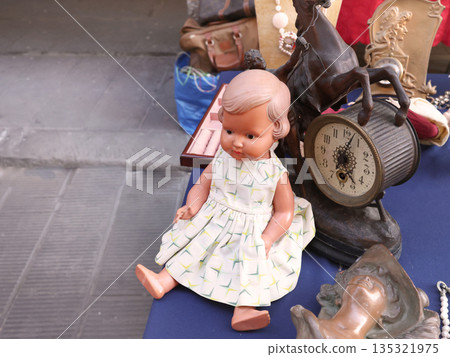 Vintage items and toys at flea market in Europe, Italy. Doll in dress and table clock. Old items and art. Vintage items and toys at flea market in Europe, Italy. Doll in dress and table clock. Old items and art. 135321975
