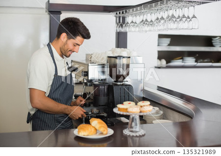 Male barista operating espresso machine behind counter with portafilter, croissants and cupcakes 135321989