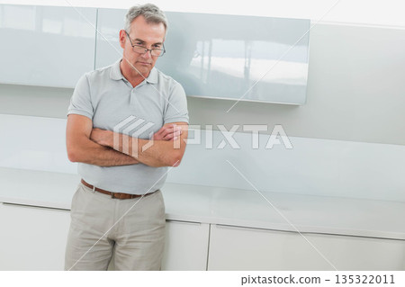 Man standing, pondering in modern kitchen wearing reading glasses near grey countertop, copy space 135322011
