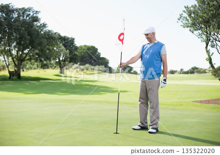 Male golfer wearing golf glove standing on green grasping flagstick by hole on fairway, copy space Male golfer wearing golf glove standing on green grasping flagstick by hole on fairway, copy space 135322020