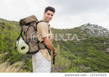 Male hiker standing on hillside trail using poles and carrying green backpack with mat, copy space Male hiker standing on hillside trail using poles and carrying green backpack with mat, copy space 135322029