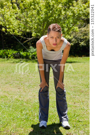 Woman pausing during outdoor workout on grassy field in public park wearing white running shoes Woman pausing during outdoor workout on grassy field in public park wearing white running shoes 135322041