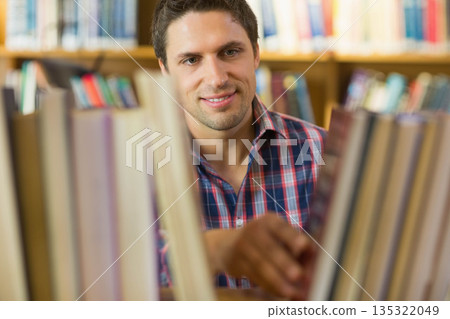 Man standing between bookshelves in library, looking through gap and selecting volume Man standing between bookshelves in library, looking through gap and selecting volume 135322049