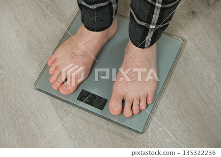 Man weighing himself on modern weighing scales at home, close-up of bare feet. 135322236