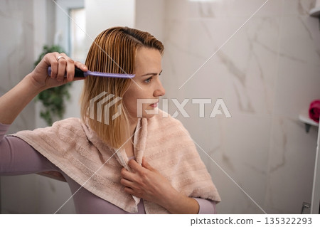 Woman combing her hair after shower in the bathroom Woman combing her hair after shower in the bathroom 135322293