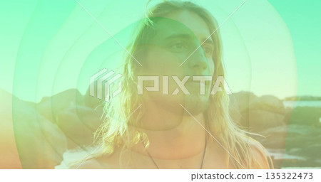 Standing adult male gazing upward at rocky shoreline, with pendant necklace and green gold overlays 135322473
