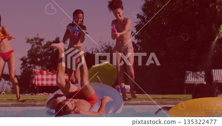 Laughing friends in swimwear spraying man reclining on tube at backyard pool, with water blasters 135322477