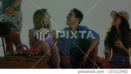 Laughing friends holding bottled drinks, grilling with spatula on beach blanket, with wicker basket Laughing friends holding bottled drinks, grilling with spatula on beach blanket, with wicker basket 135322482