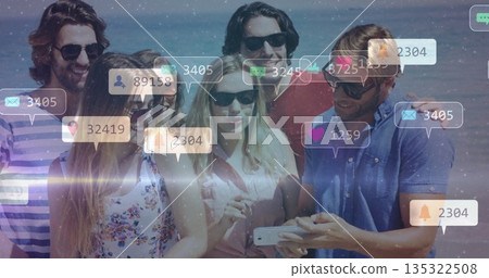 Leaning in six friends wearing sunglasses viewing smartphone on beach, with social media icons 135322508
