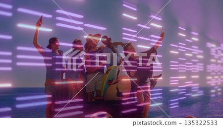 Five friends standing on sandy beach holding smartphones and bottles, with cooler rig and surfboard 135322533