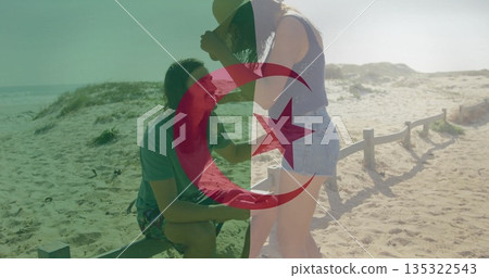 Kneeling man presenting ring box to woman adjusting sunhat on beach path, with fence and dunes Kneeling man presenting ring box to woman adjusting sunhat on beach path, with fence and dunes 135322543
