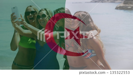 Smiling group of four women taking selfie at sandy shore, with smartphone and crescent star symbol 135322553