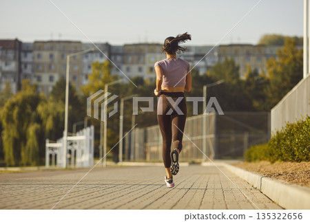 Young woman jogging in urban park, rear view runner training outdoors on sunny day Young woman jogging in urban park, rear view runner training outdoors on sunny day 135322656
