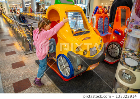 Little girl riding coin operated toy car attraction in shopping mall kids area. Childhood entertainment moment, family leisure activity and everyday fun experience in real life commercial environment 135322914