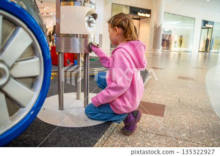 Little girl standing near gemstone vending machine and waiting for random stone in shopping mall kids area. Childhood curiosity moment, family leisure experience in real life commercial environment 135322927