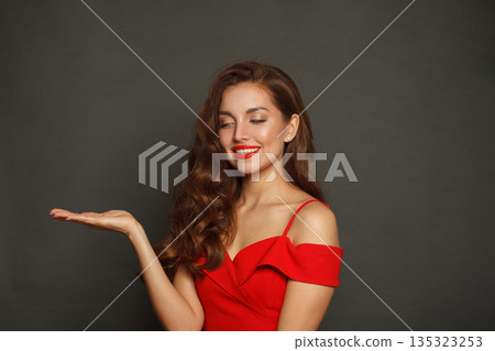 Lovely model woman holding empty open palm hand and smiling on black background Lovely model woman holding empty open palm hand and smiling on black background 135323253