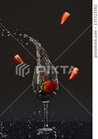 Several strawberries falling into a glass and splashing water 135323562
