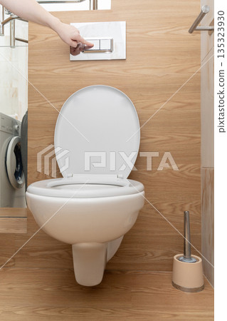 Hand pressing dual flush buttons on a ceramic wall-hung toilet, promoting hygiene and water saving in a modern bathroom Hand pressing dual flush buttons on a ceramic wall-hung toilet, promoting hygiene and water saving in a modern bathroom 135323930