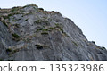 A low-angle detailed view of a steep rocky cliff face reinforced with a heavy-duty steel wire mesh netting designed to prevent rockfalls and landslides. 135323986