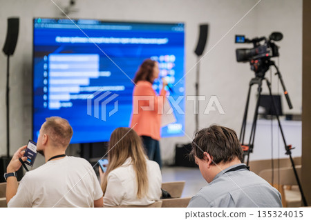Conference presentation in a studio style room with audience watching as camera records 135324015