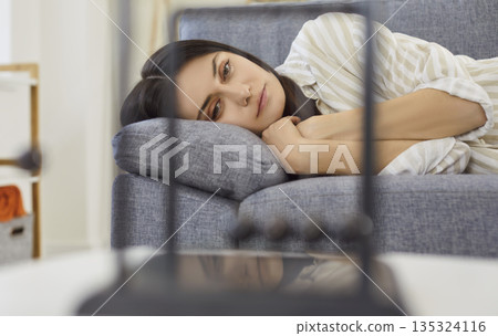 Frustrated young woman looking at Newton's cradle balance balls lying on sofa at home Frustrated young woman looking at Newton's cradle balance balls lying on sofa at home 135324116