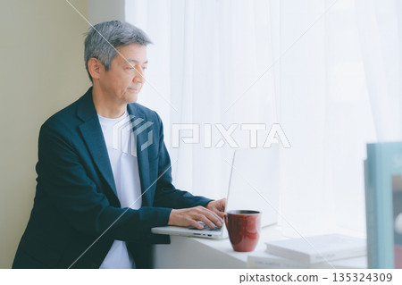 A man working on a computer by the window A man working on a computer by the window 135324309
