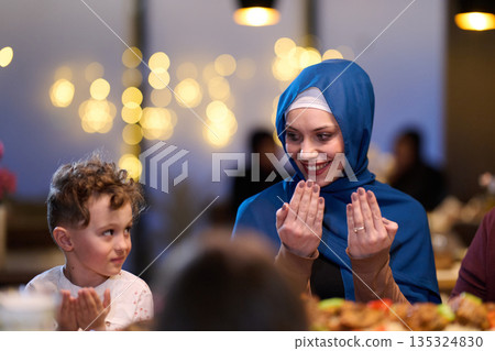 Muslim Mother and Son Praying Before Iftar Meal at Home or Restaurant - Religious Traditions, Ramadan Kareem, and Family Bonding Concept. 135324830