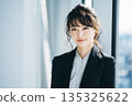Portrait of a young Japanese woman looking at camera while standing by a window in an office 135325622